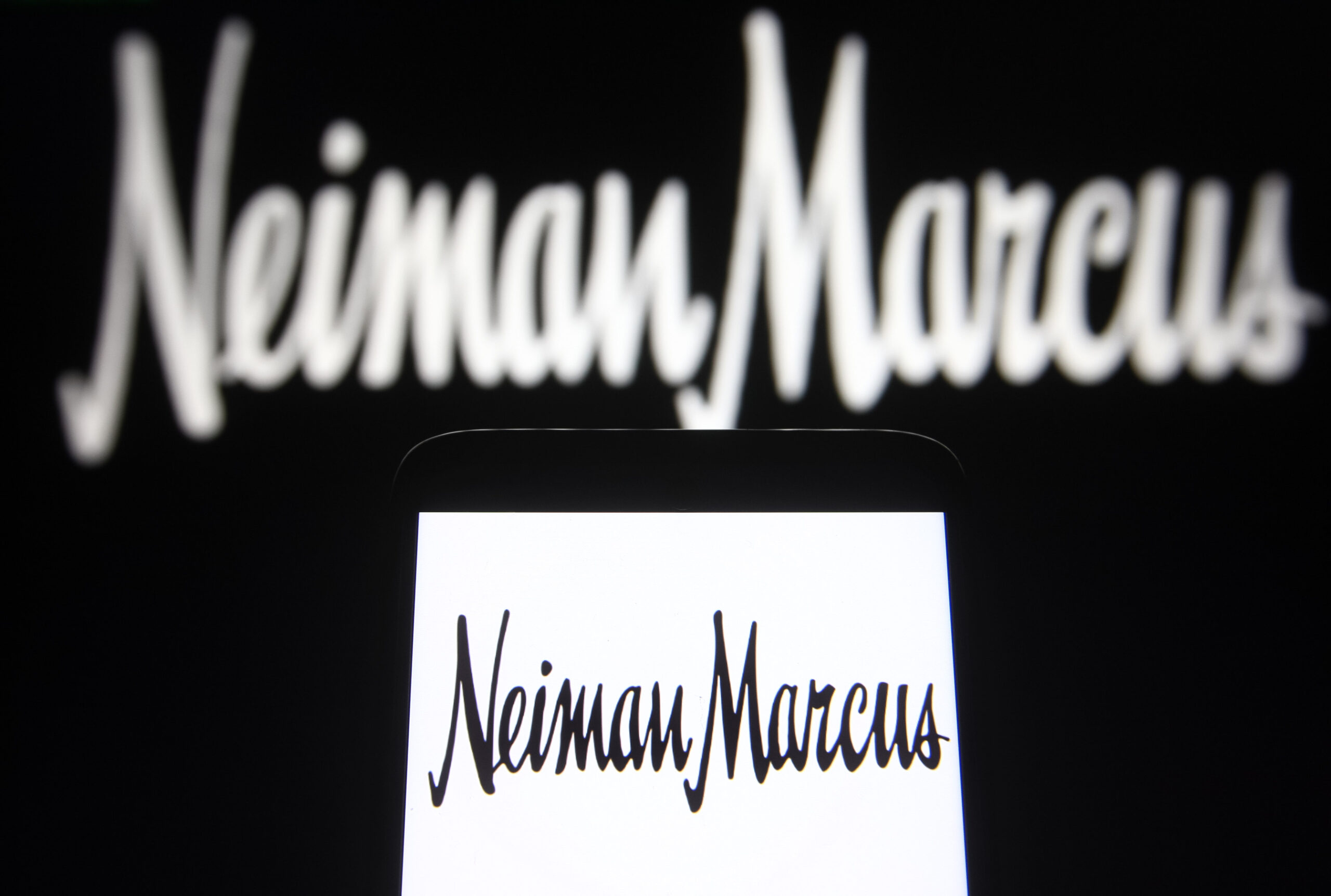 In this photo illustration a Neiman Marcus Group, Inc. logo is seen on a smartphone and a pc screen.