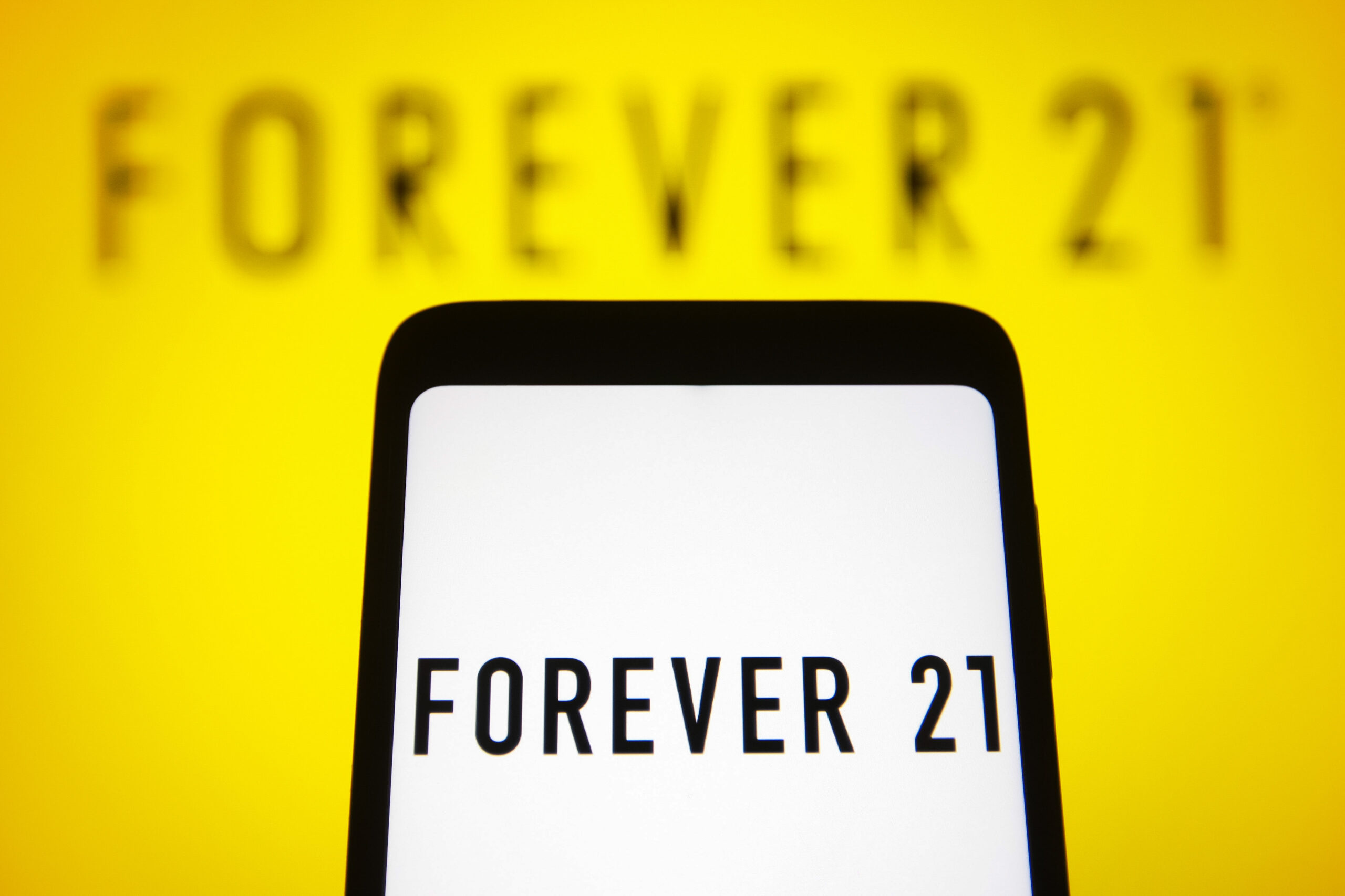 In this photo illustration, logo of Forever 21, a fast fashion retailer is seen on a smartphone and in the background.