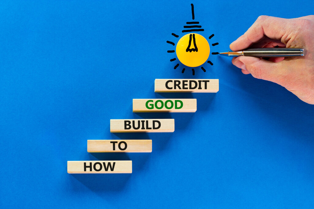 Build good credit symbol. Wooden blocks with words How to build good credit. Light bulb icon. Businessman hand with pen. Beautiful blue background, copy space. Business and build good credit concept.